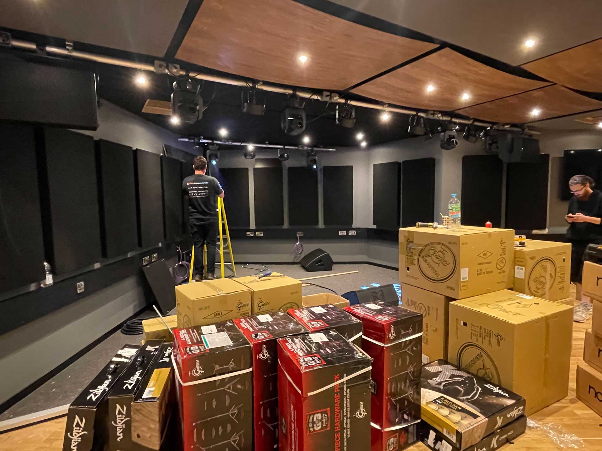 Studio fit-out in progress with equipment boxes and an installer on a ladder