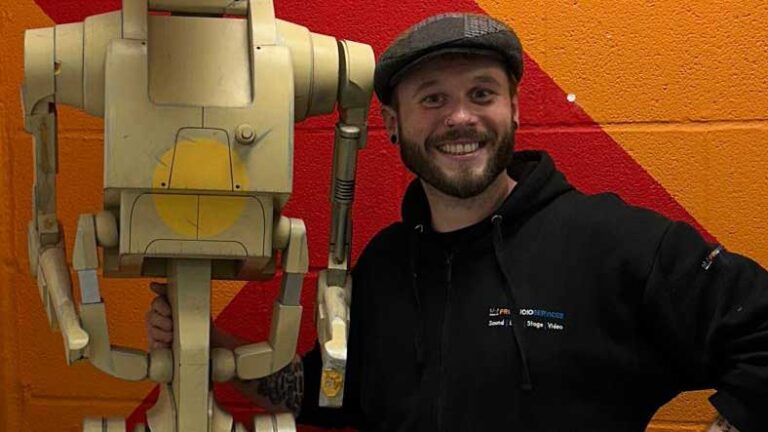 Tom Foulkes in a cap, smiling in front of red equipment