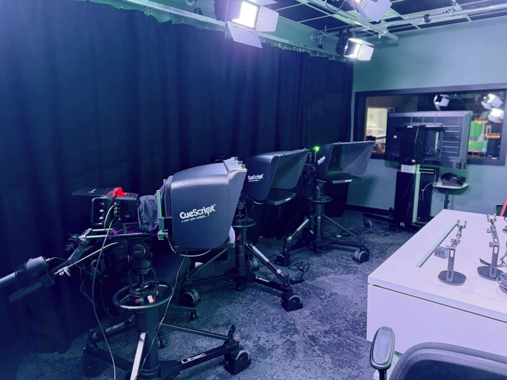 Studio floor with black drapes, cameras and monitors in a broadcast suite