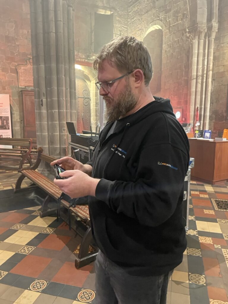 Sound engineer in a black hoodie checking a tablet inside a church