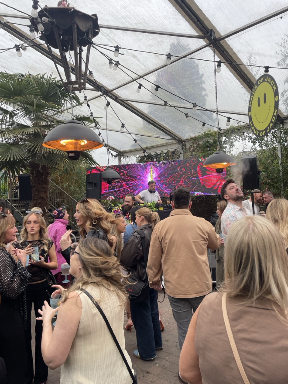 DJ syanding on a stage playing music with a video wall behind him. People are dancing in front of him.