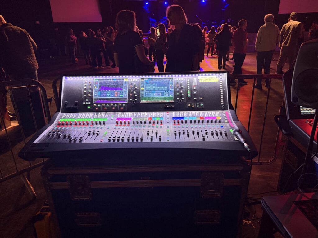 Digital mixing console at front of house in a venue with stage lighting behind