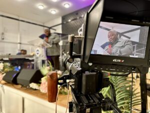 Camera filming a man speaking on stage at Fountain of Grace Worship Centre