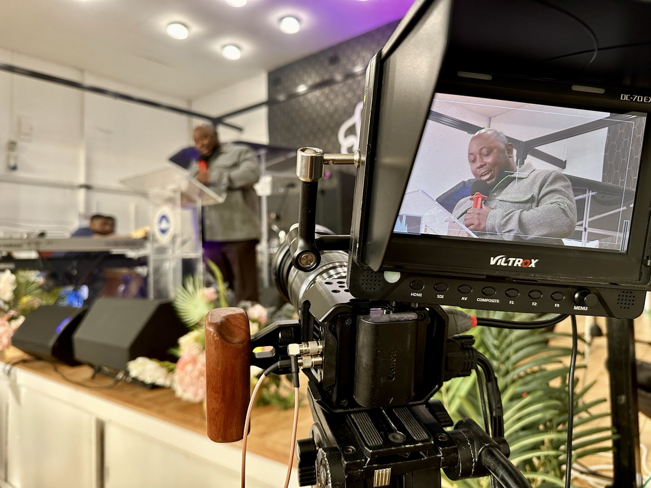 Camera filming a man speaking on stage at Fountain of Grace Worship Centre