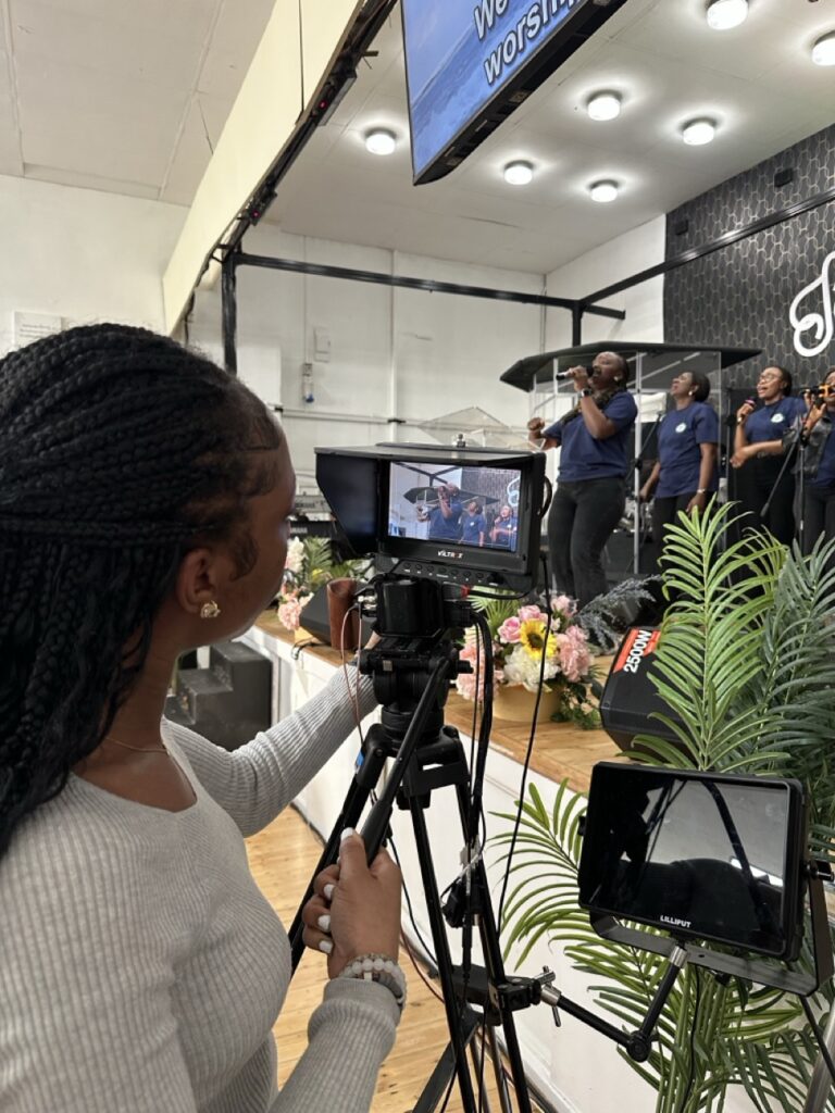 Camera operator at a tripod filming in a worship centre with screens above