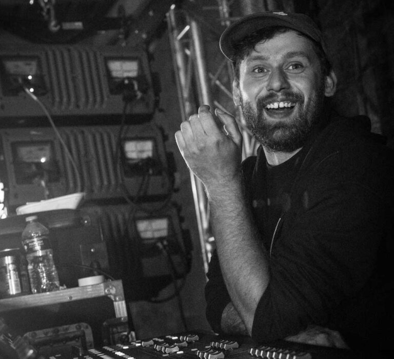 Jake Jones smiling beside a mixing desk, in black and white
