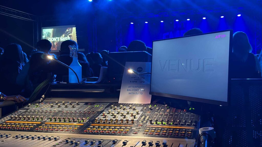 Mixing desk at front of house with a video screen and a blue-lit stage beyond