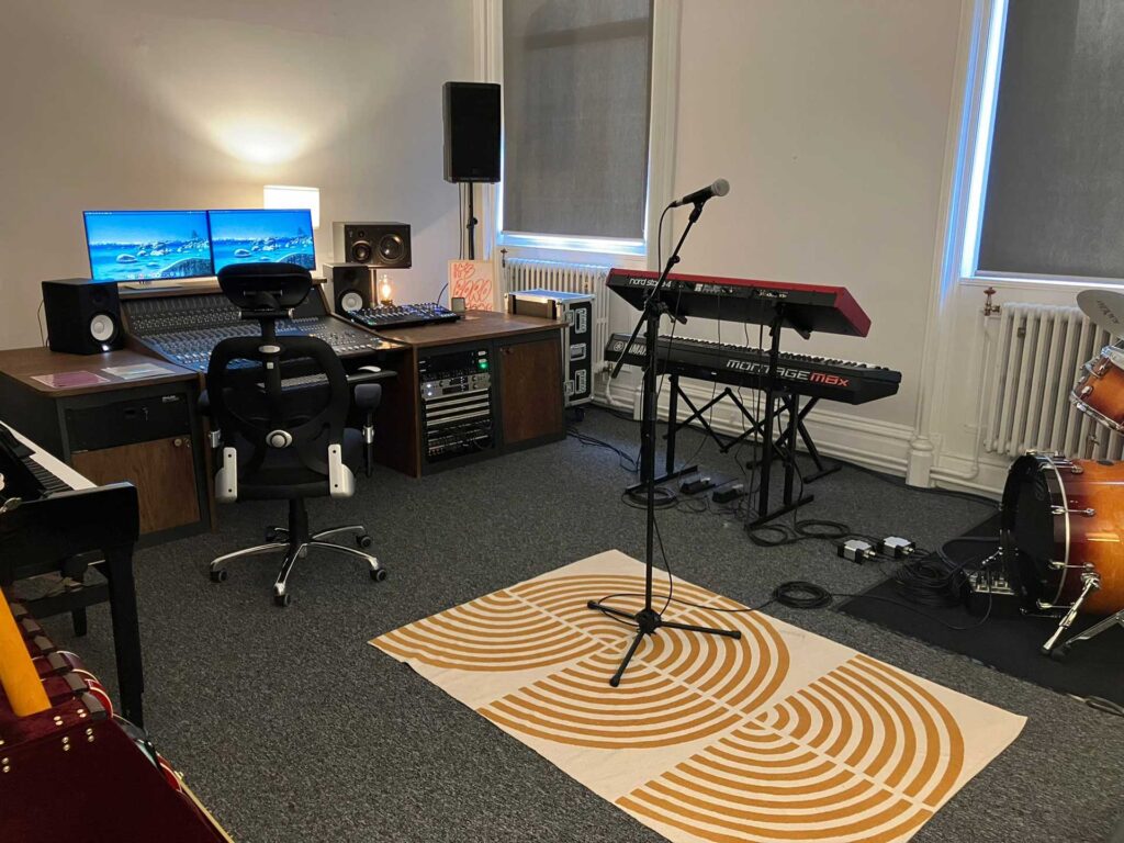 Looking into the wider space of the studio installation with the workstation in background alongside keyboards setup for use.