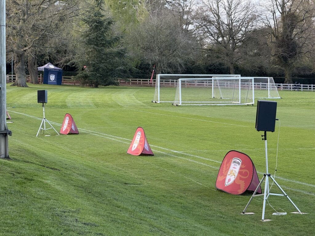 Football pitch with cones, a speaker on a tripod and goalposts in the background