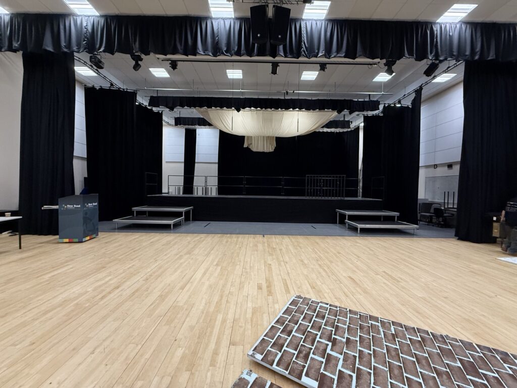 Hall with black curtains, a stage and a polished wooden floor set up for the show