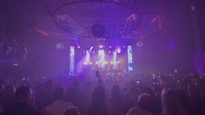 A band playing on a stage with lights behind them that light up the audience in front.