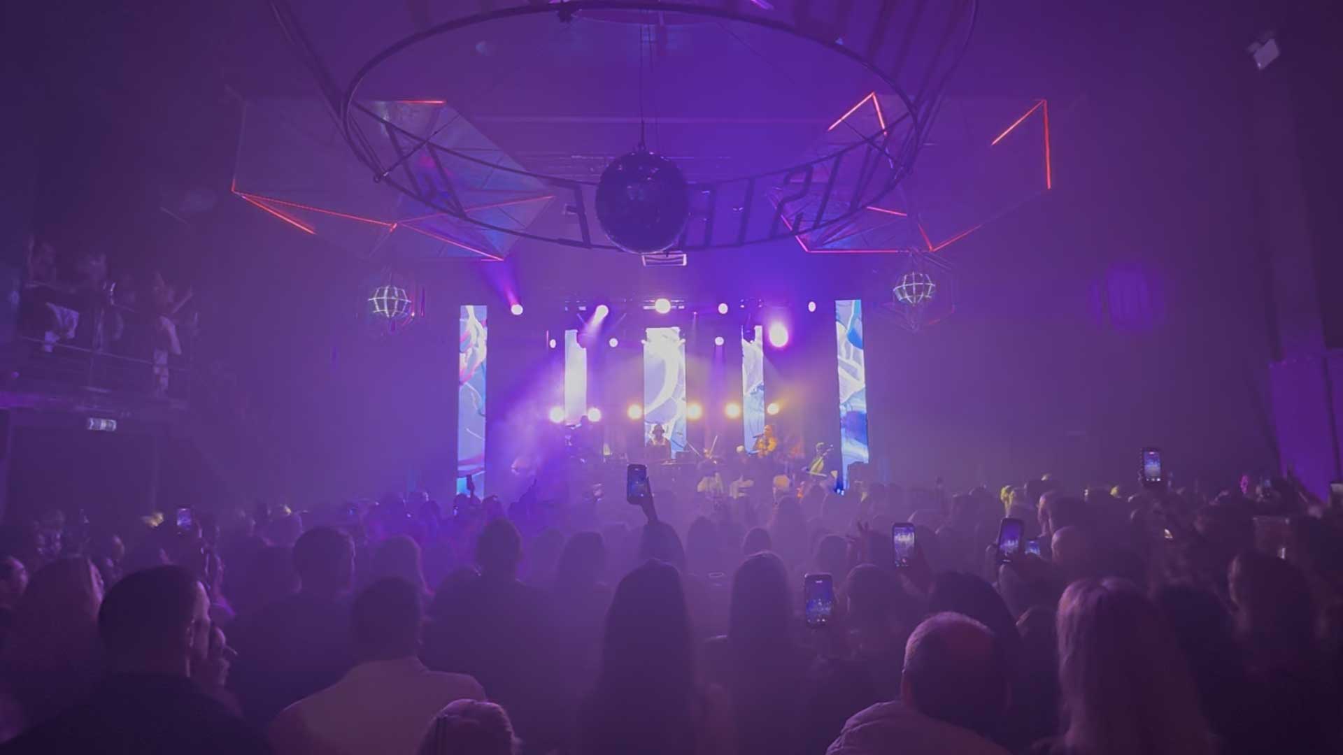 A band playing on a stage with lights behind them that light up the audience in front.