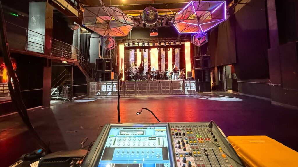 Venue main room with a mixing desk in the foreground and a purple-lit ceiling