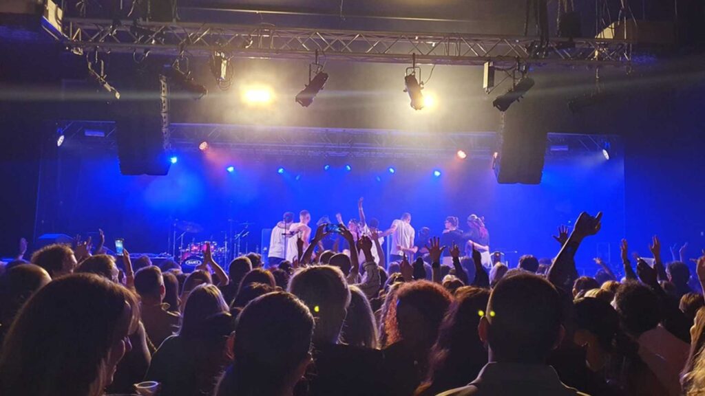 Crowd with raised arms in front of a stage lit in blue