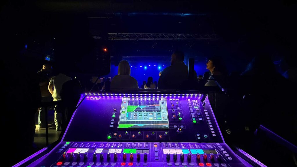 Digital mixing console lit in purple and green at front of house