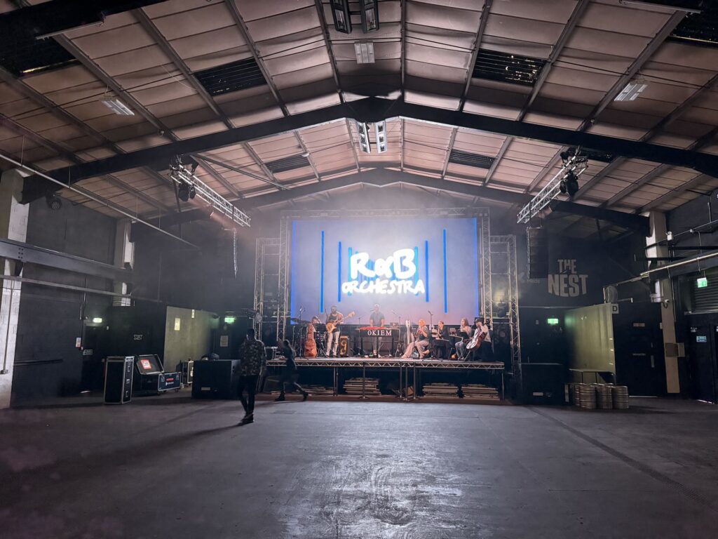 Large empty industrial venue with a lit stage and screen at the far end