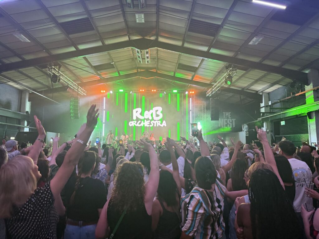 Crowd with raised hands inside an industrial building under green stage lighting
