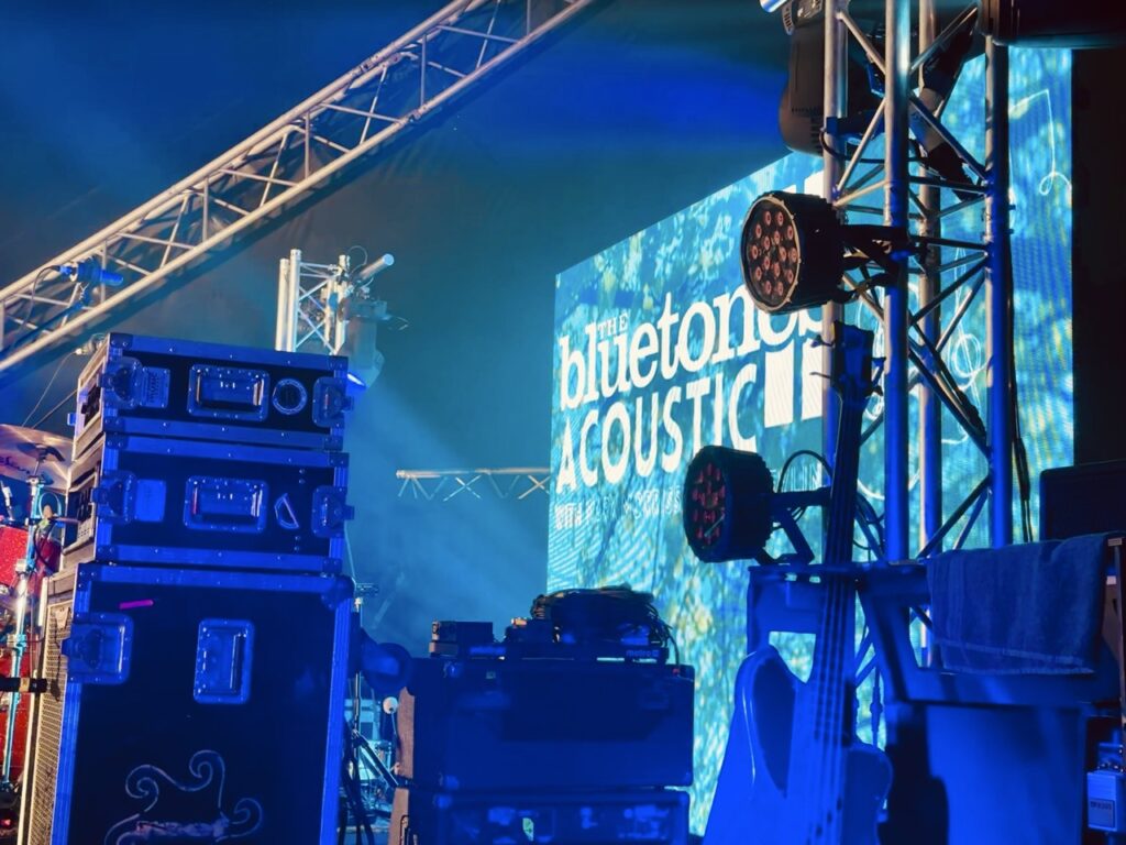 Line array speaker stacks and an LED screen on a stage rig lit in blue at Loopfest