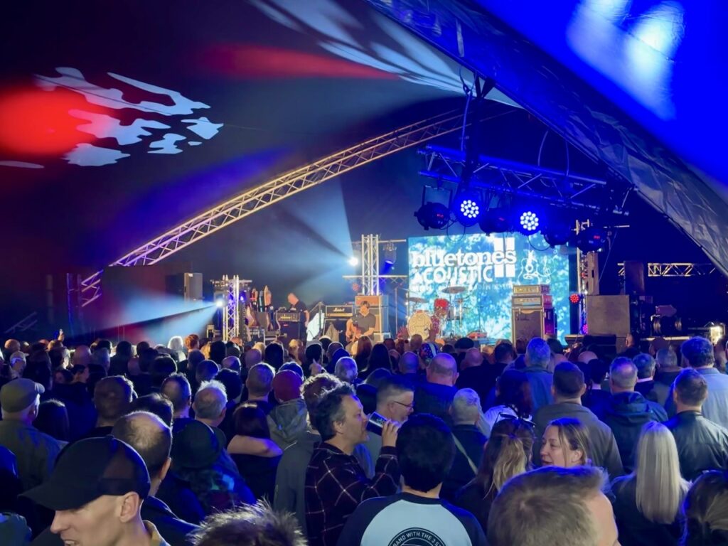 Crowd gathered in front of a blue-lit stage with an LED screen at Loopfest