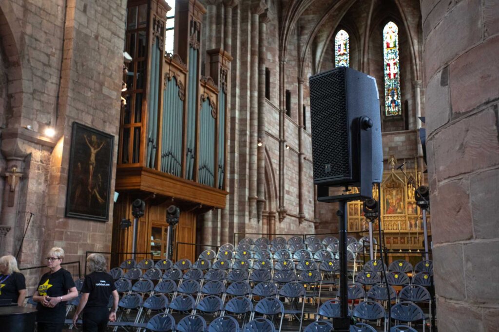 Speaker on a stand and rows of chairs in a church with the organ behind