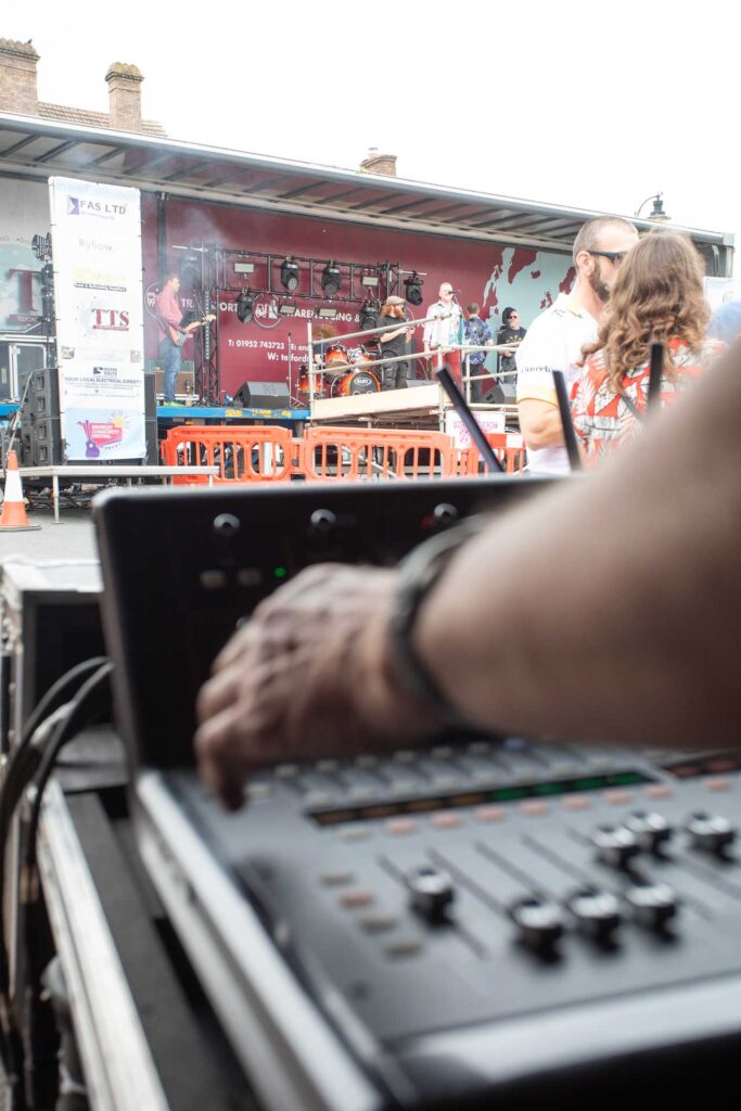 Hand adjusting a small mixing desk with a stage and spectators behind