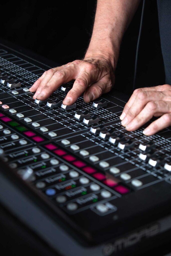 Close-up of hands on the faders of a mixing console