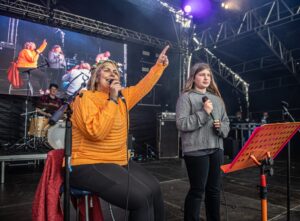 A lady and her daughter singing on a stage with a video wall behind them