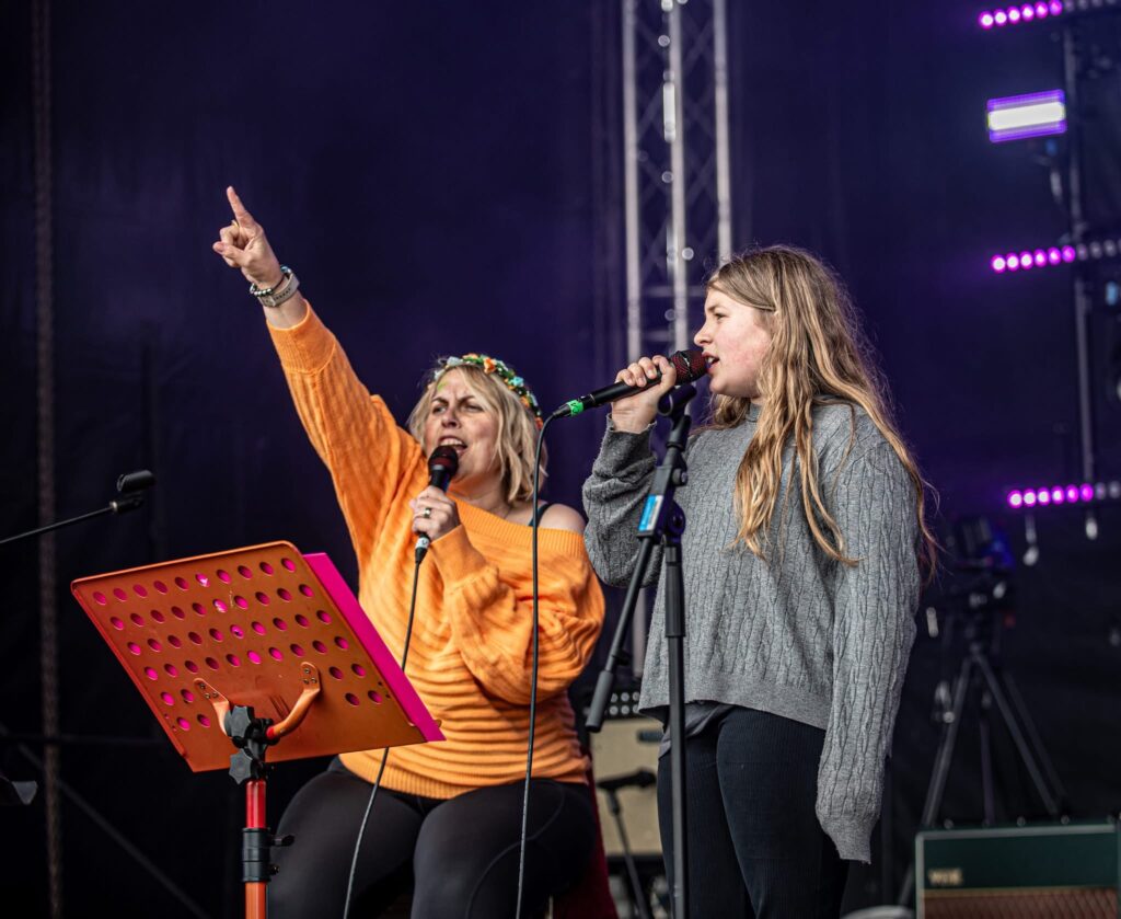 Two singers on stage, one pointing upwards, beside a music stand