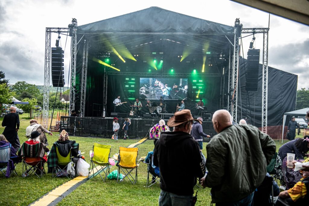 Covered stage with green lighting and spectators on camping chairs in front