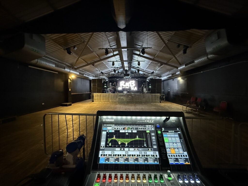 Digital mixing console at front of house in a hall with the stage in the distance