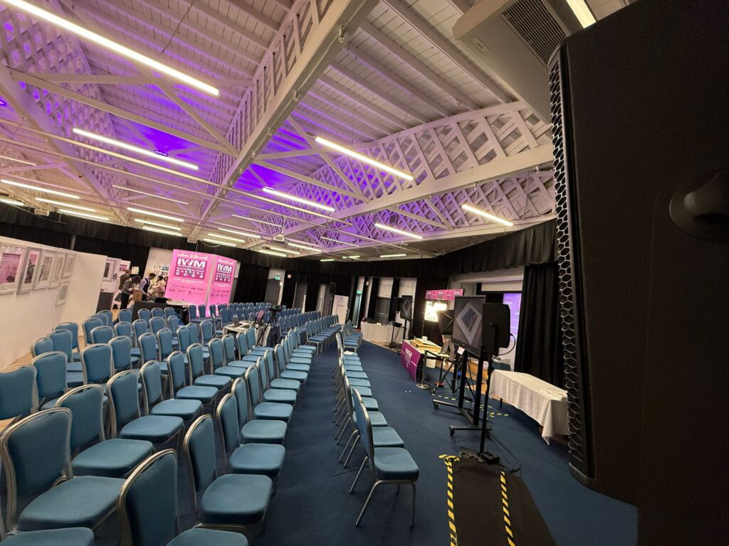 Rows of blue chairs in a hall with a lit ceiling, set up for the event
