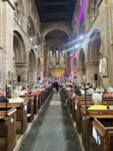 People sat in pews in Shrewsbury Abbey watching a choir sing on stage at the Power of Song charity event