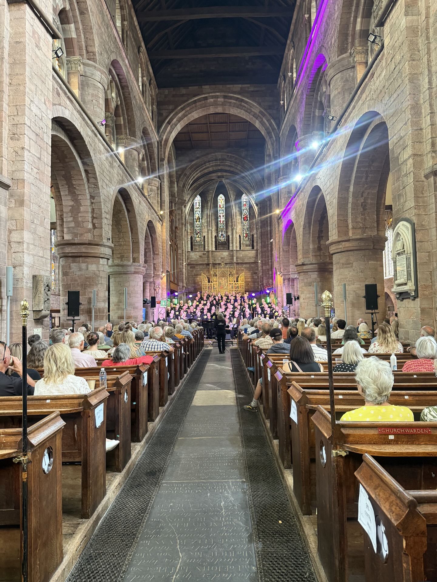 People sat in pews in Shrewsbury Abbey watching a choir sing on stage at the Power of Song charity event