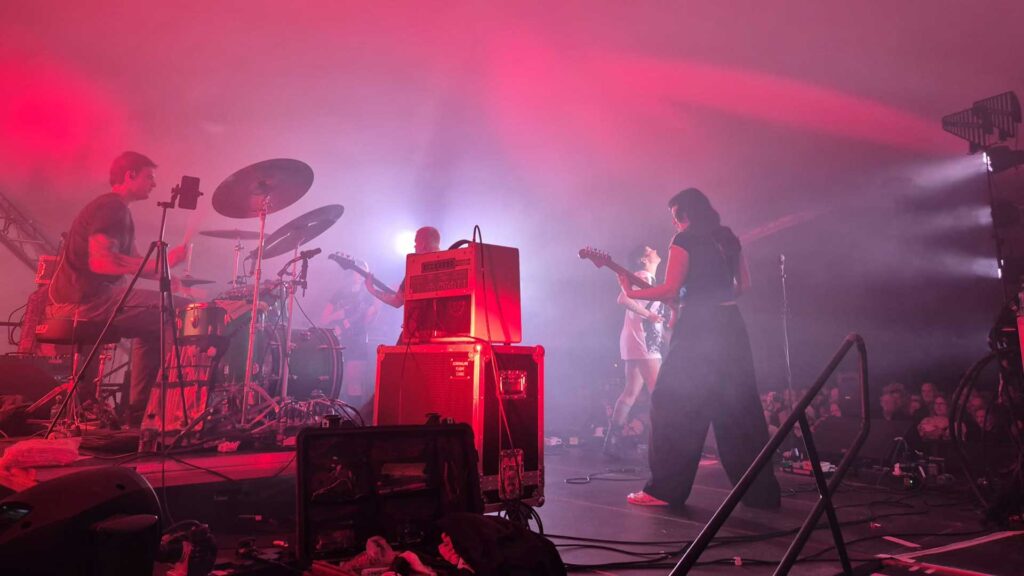 Drummer and guitarist on a stage lit in red and pink with haze
