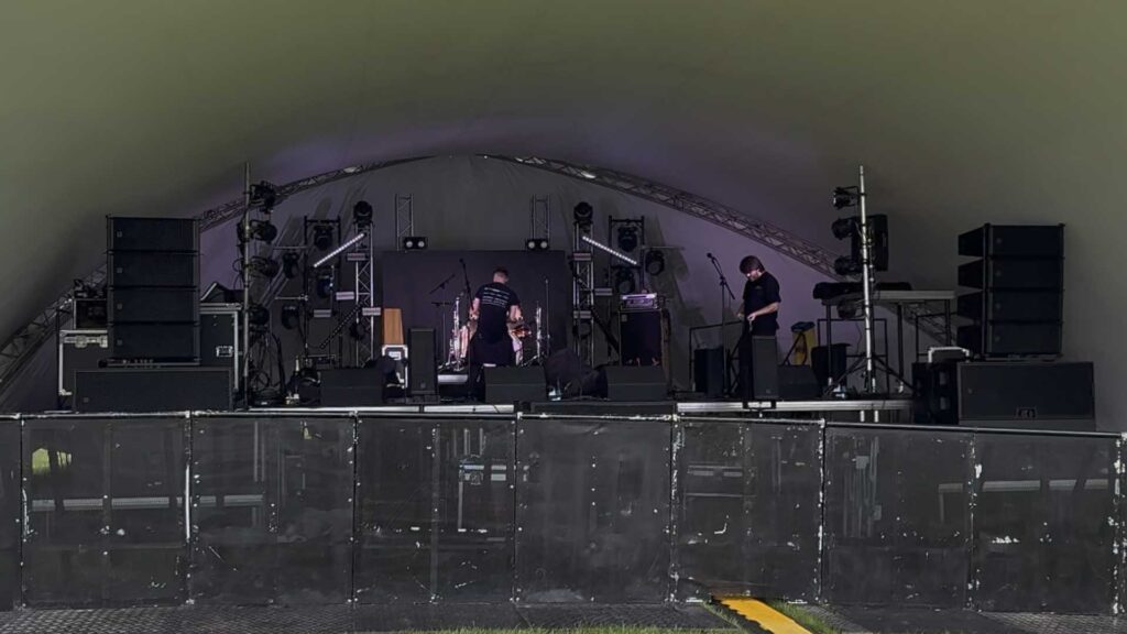 Band playing on a stage inside a large tent with speaker stacks either side