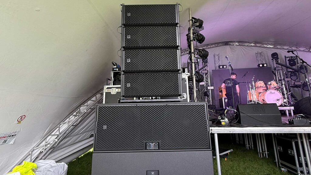 Line array speaker stack beside the stage with crew seated behind it