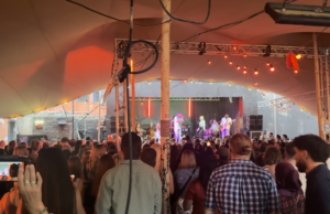 People stood under a canopy watching a band play on a stage.