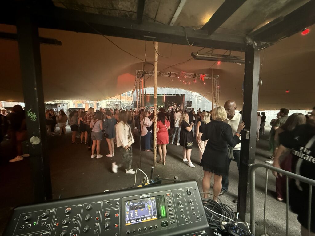 Mixing desk in the foreground with a crowd dancing under the marquee