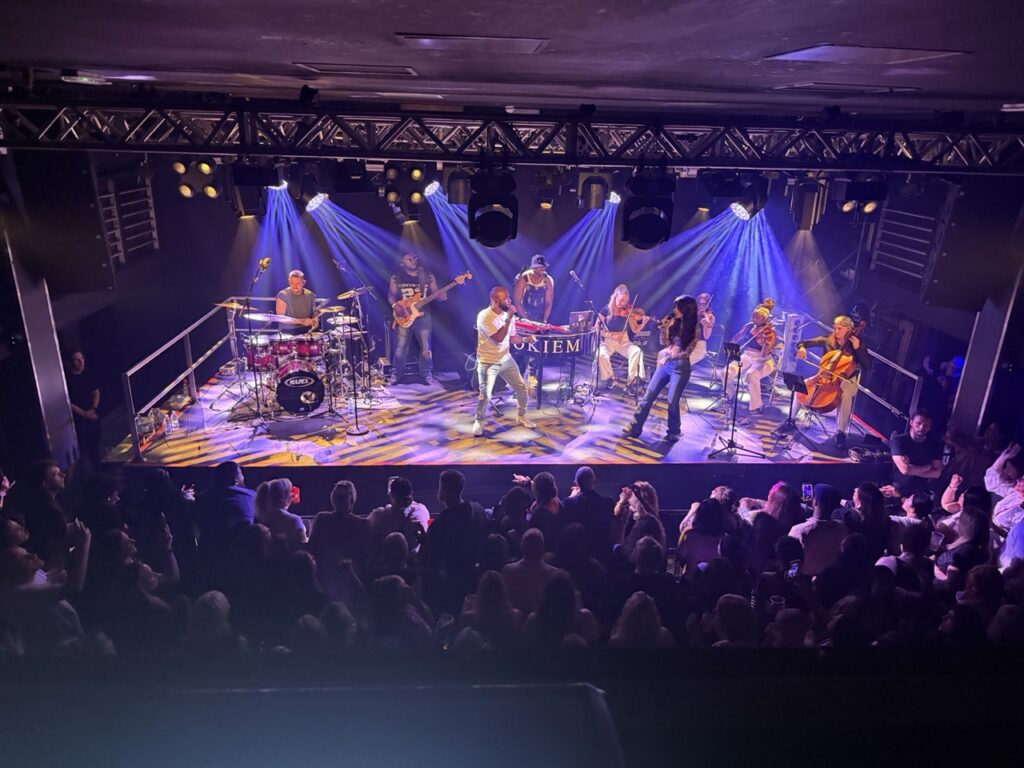 Orchestra on a blue and red-lit stage with the crowd in front