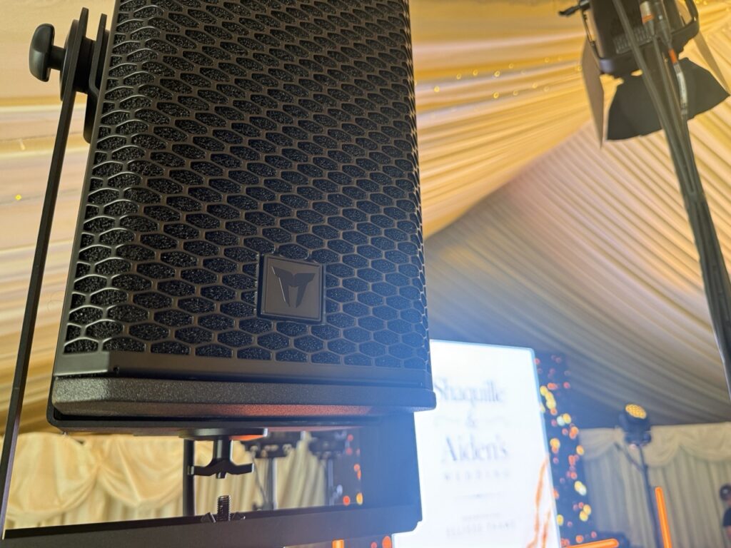 Line array speaker flown from a marquee frame under warm lighting