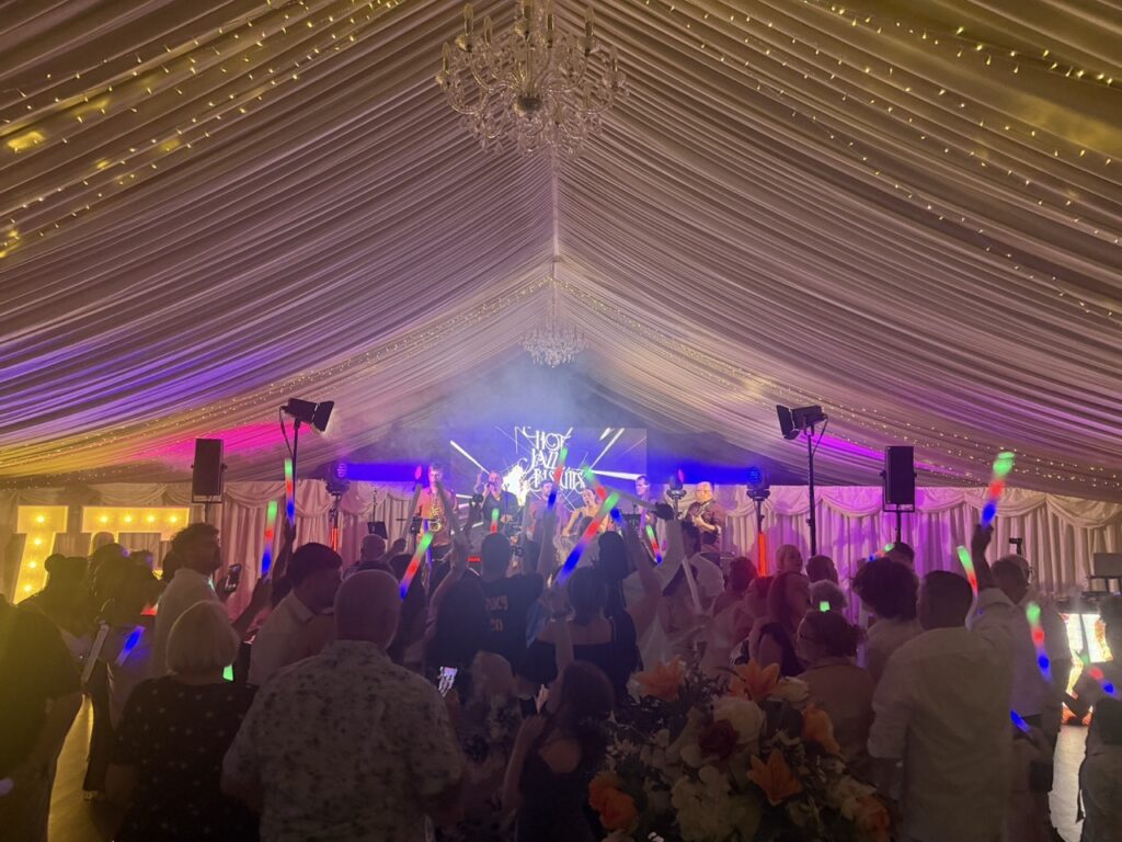 Wedding guests dancing in a marquee with white drapes and warm lighting