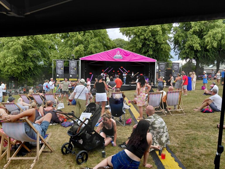 Crowd on camping chairs on the grass in front of a pink-roofed stage