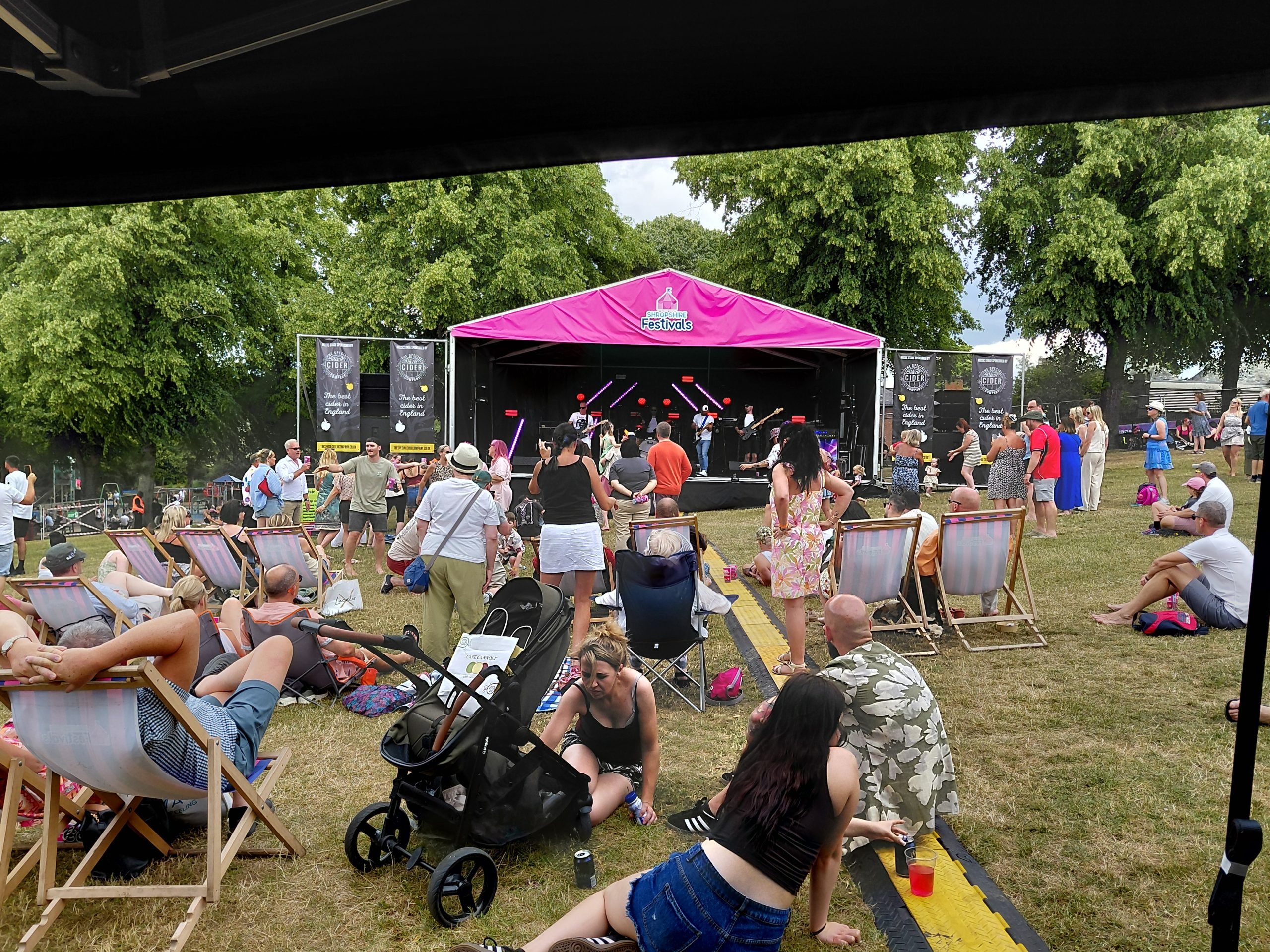 Crowd on camping chairs on the grass in front of a pink-roofed stage