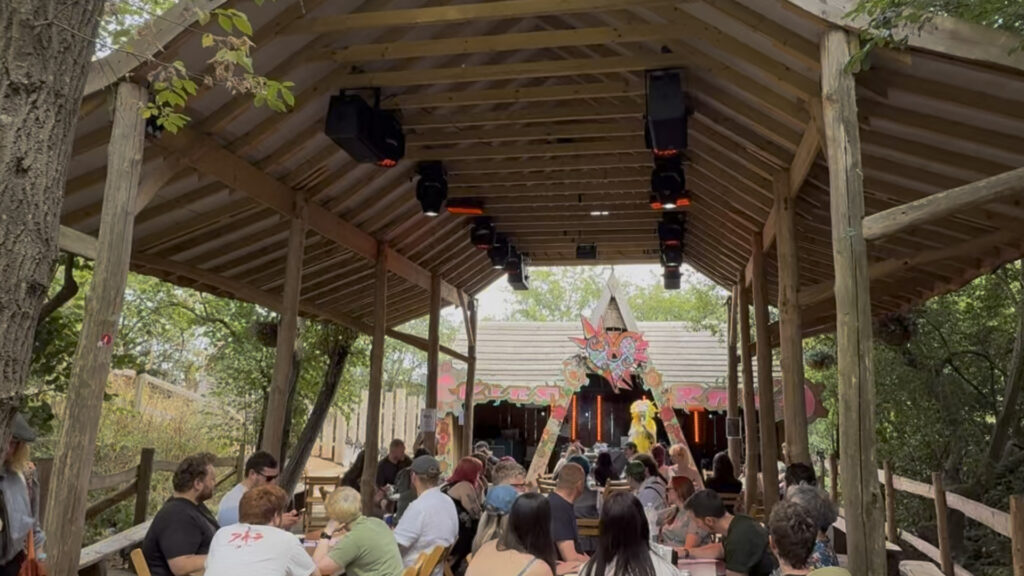 Wooden-roofed pavilion stage with lighting and a crowd gathered in front