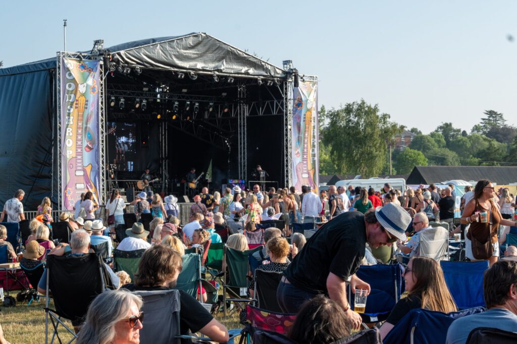 Festival stage under a black canopy with the crowd in front and a camera operator at the side