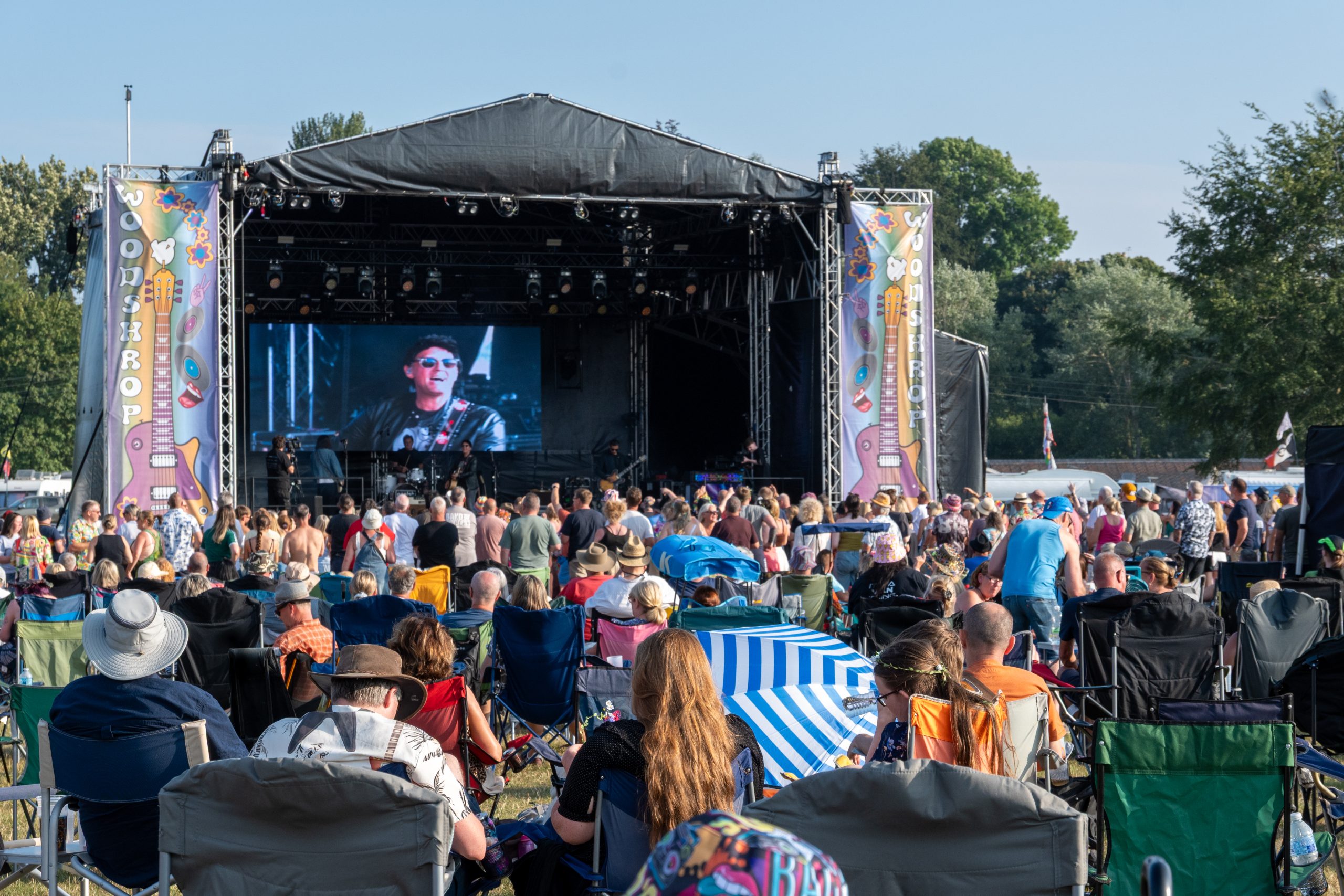 A large audience of people watch a man singing on a stage. The mans image is being live streamed to a video wall at the back of the stage.