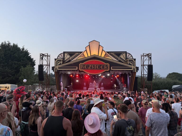 A large audience of people watch Eva Lazaras sing on a stage. Lights from the stage shine out behind her .
