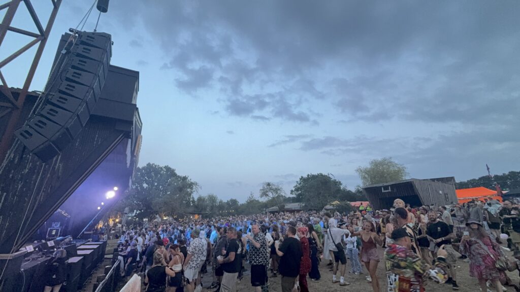 Speaker towers and a stage seen across the festival field at dusk