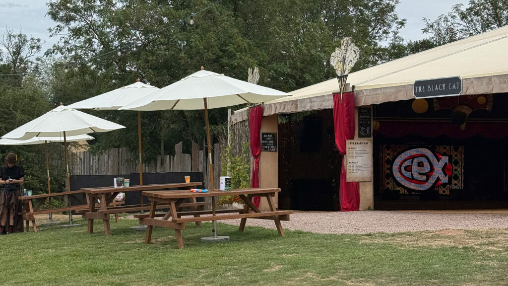 Outdoor bar and picnic tables with parasols in front of the marquee stage