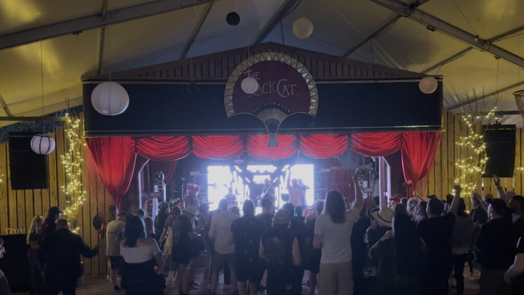 Marquee stage with a red and black backdrop under warm lights and a crowd in front